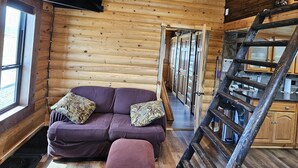 A log cabin interior with a wooden ceiling, a purple sofa with patterned cushions, a wooden staircase, and a kitchen area with cabinets. - Reboot, Recover, Recreate…Centrally located 20 acre Mill Creek getaway cabin! (Anaconda)
