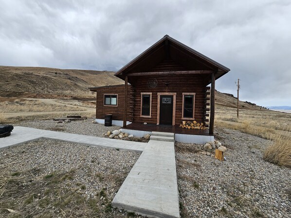 A rustic log cabin with a porch, a small attached structure, and a gravel driveway. - Reboot, Recover, Recreate…Centrally located 20 acre Mill Creek getaway cabin! (Anaconda)