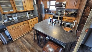 A kitchen with wooden cabinets, a granite countertop, stainless steel appliances, and a bar stool. - Reboot, Recover, Recreate…Centrally located 20 acre Mill Creek getaway cabin! (Anaconda)