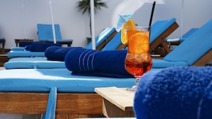 Zona junto a la piscina con sillones azules y una mesa de madera con una bebida.