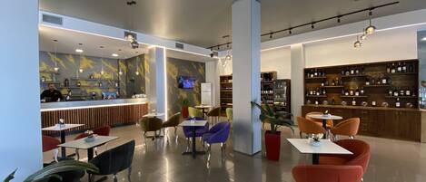 Un restaurante moderno con zona de bar, diferentes distribuciones de mesas y una exhibición de vinos.
