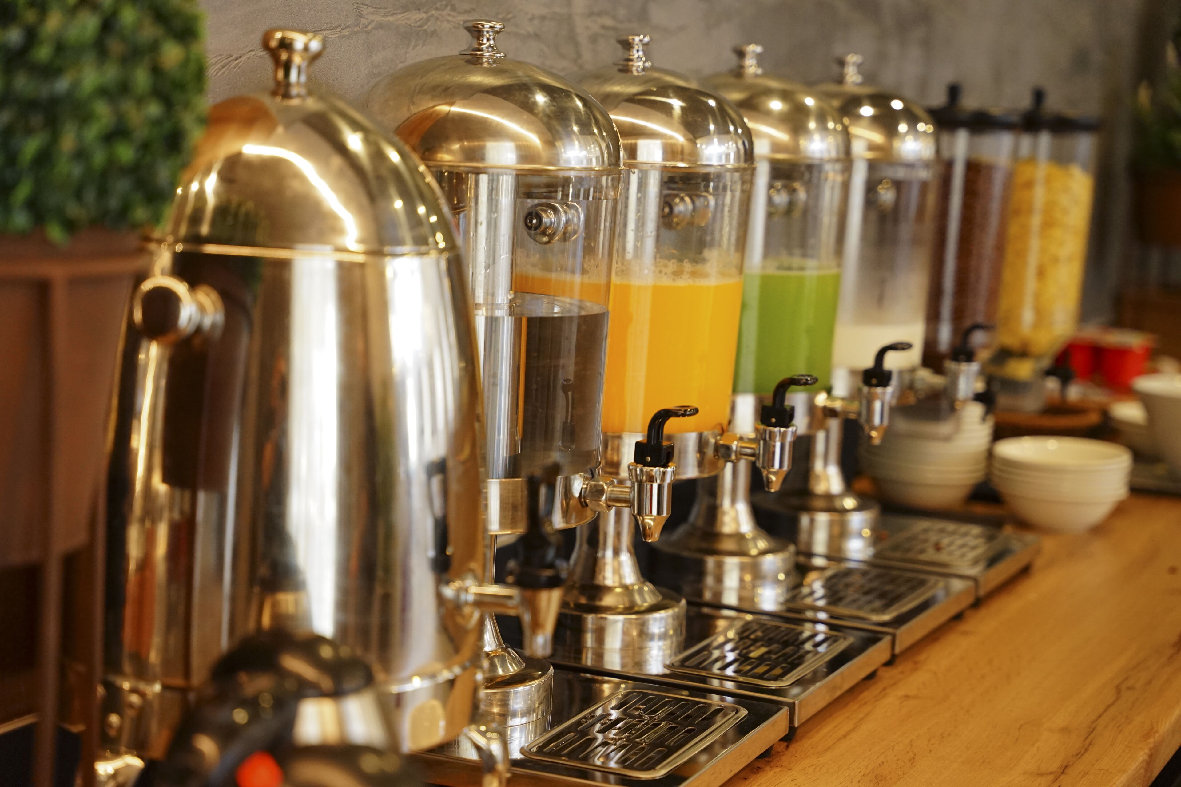 Una hilera de dispensadores de bebidas de acero inoxidable con recipientes transparentes, cada uno conteniendo una bebida de color diferente.