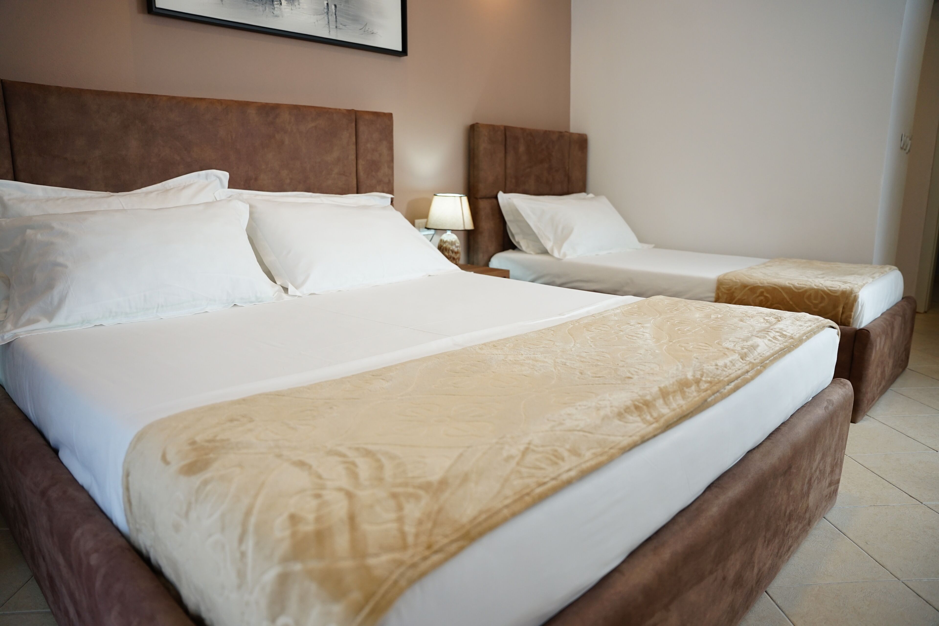 Een hotelkamer met twee bedden, elk voorzien van witte lakens en een bruin hoofdeinde. Daartussen bevindt zich een nachtkastje met een lamp.