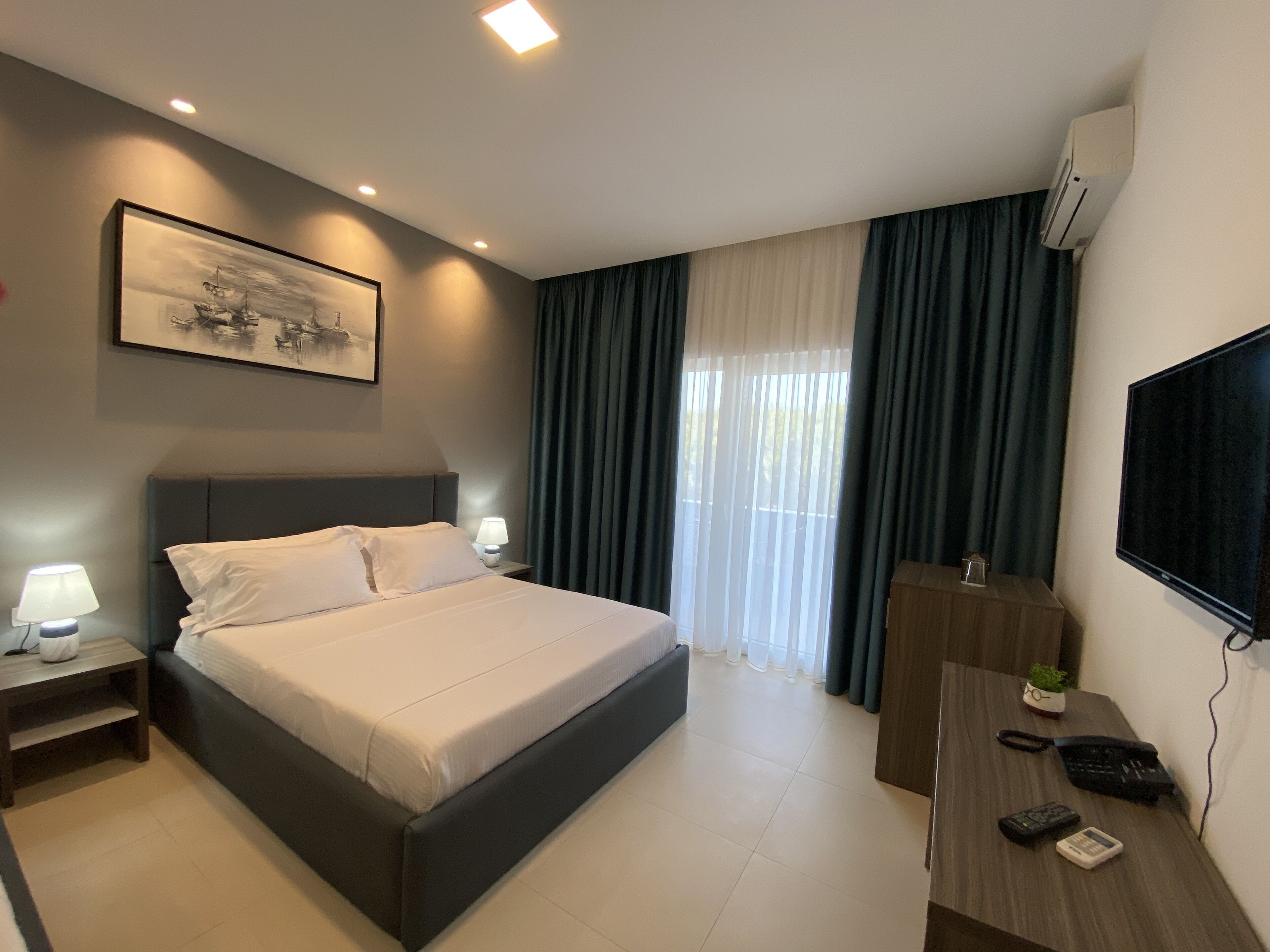 A hotel room with a bed, a desk, a TV, and a window with curtains.