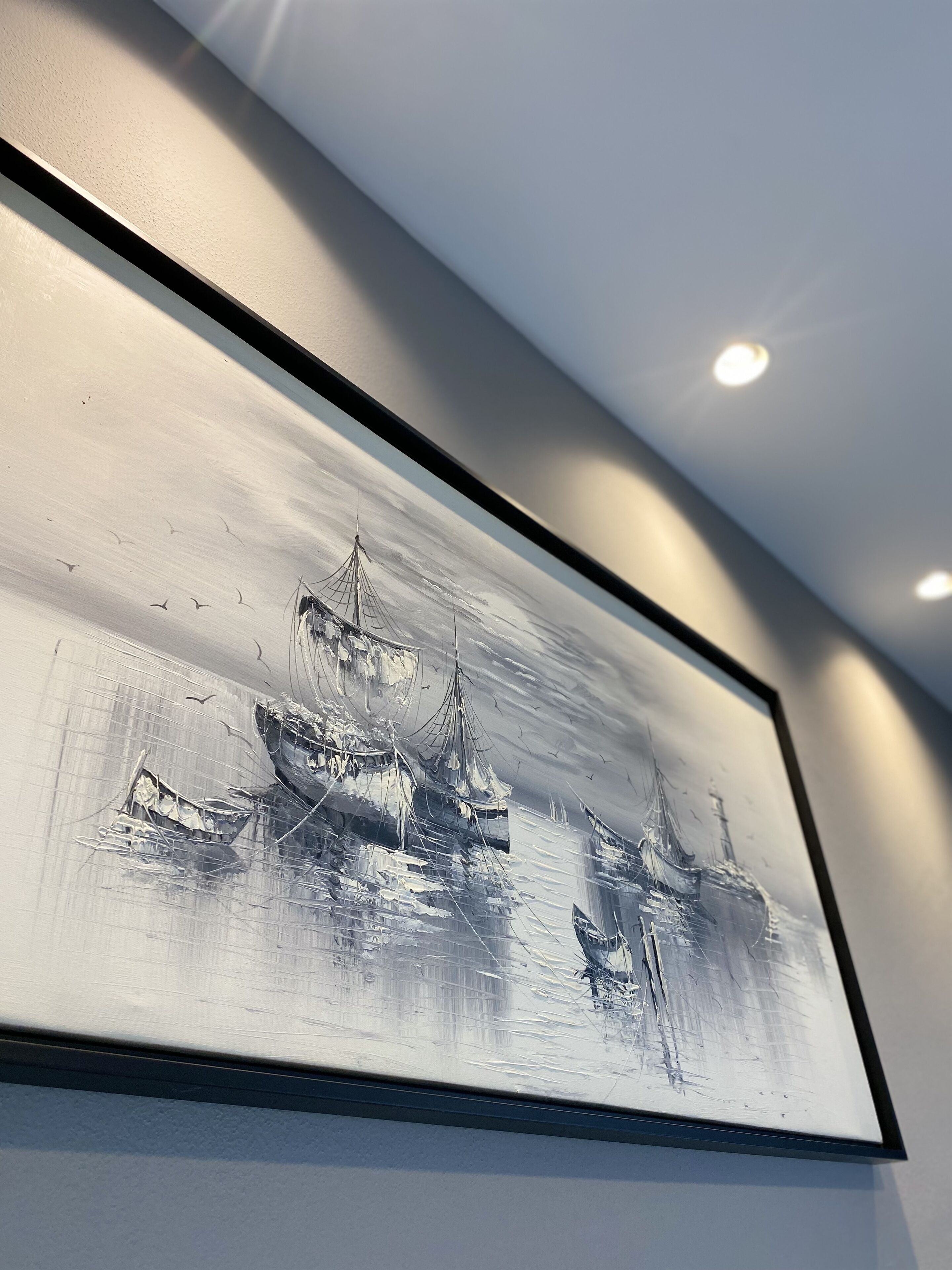 A framed black and white painting of a shipwreck on a wall.