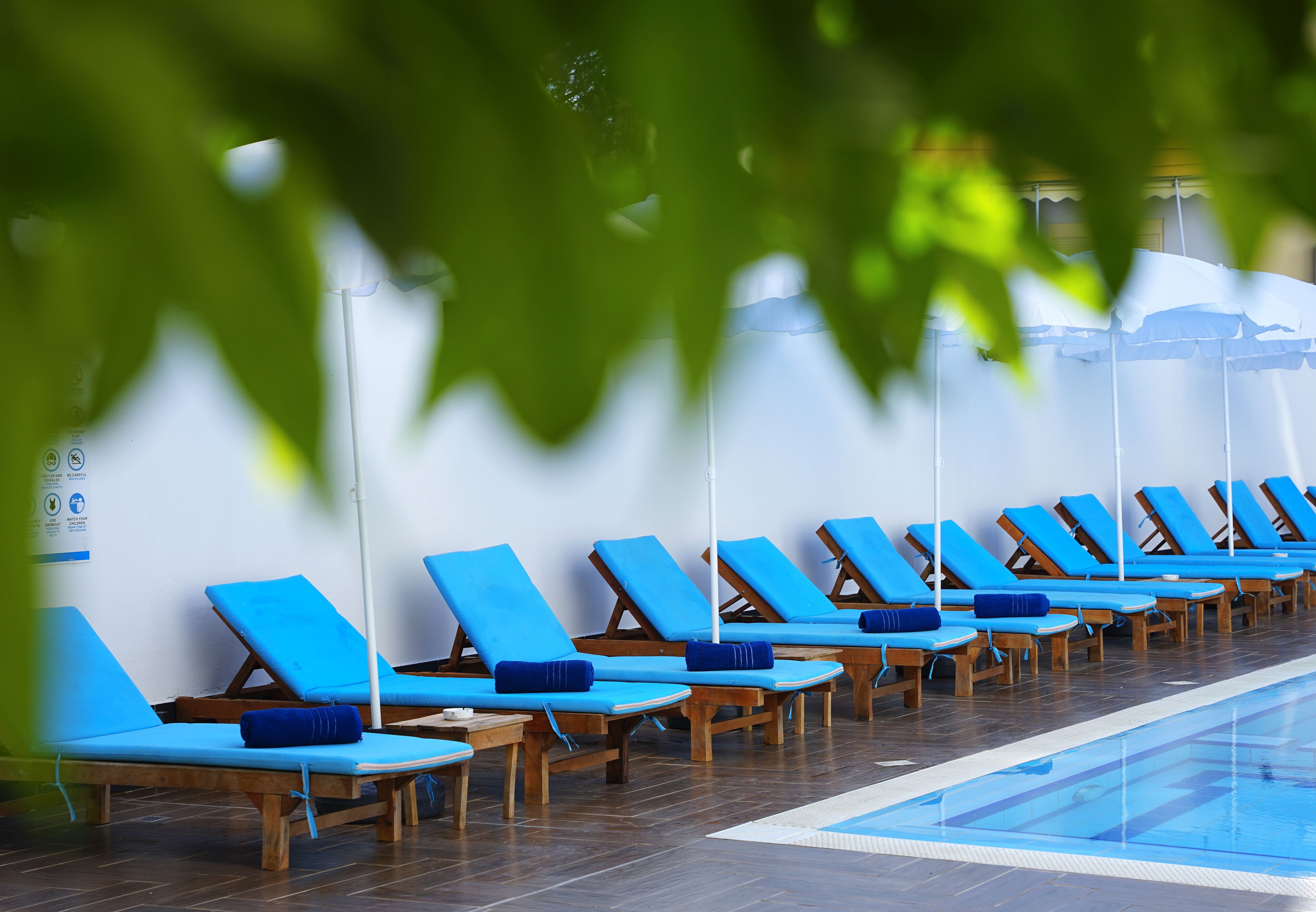 A row of blue lounge chairs with white umbrellas, arranged along a poolside.