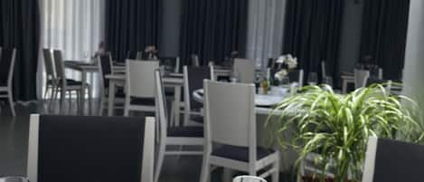 A dining area with tables set for two, featuring white tablecloths, clear glassware, and a potted plant.