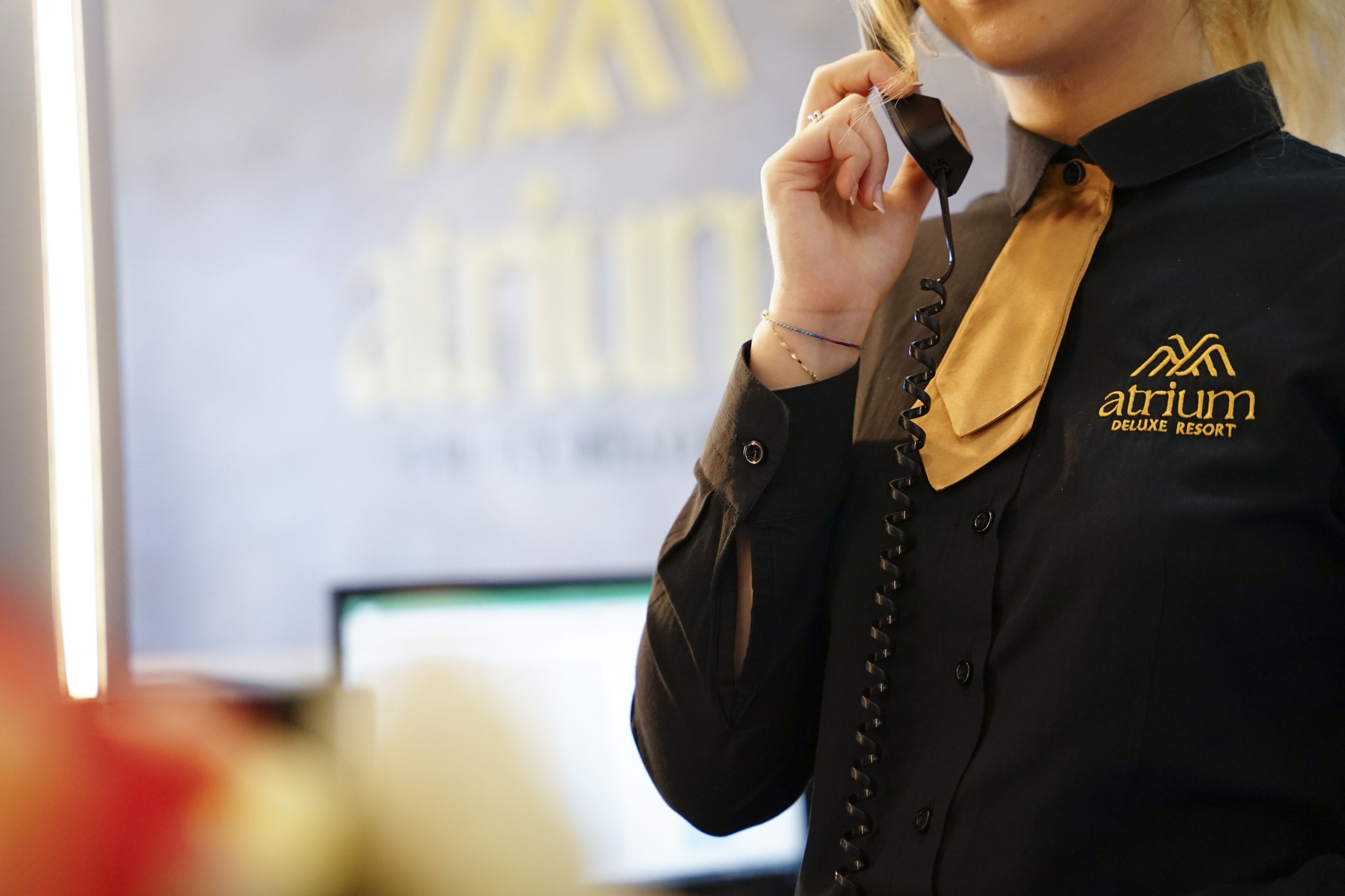 Una persona con una camisa negra con cuello dorado y un logotipo que dice 'atrium DELUXE RESORT'.