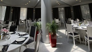 Un comedor moderno con una columna central, mesas dispuestas con manteles blancos y plantas en macetas.