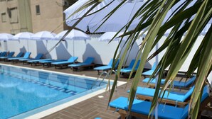 Un área de piscina con sillones reclinables azules y sombrillas.