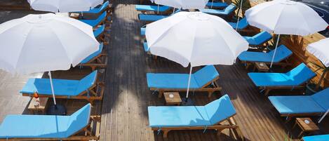 Una terraza con múltiples tumbonas y sombrillas blancas.
