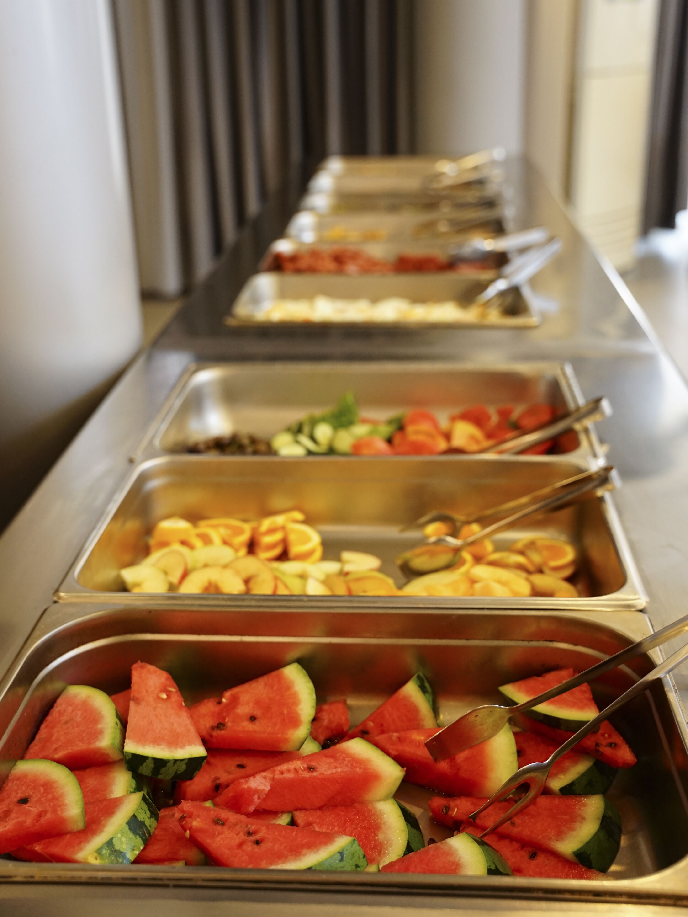 A buffet line with various food items including watermelon slices and other fruits.