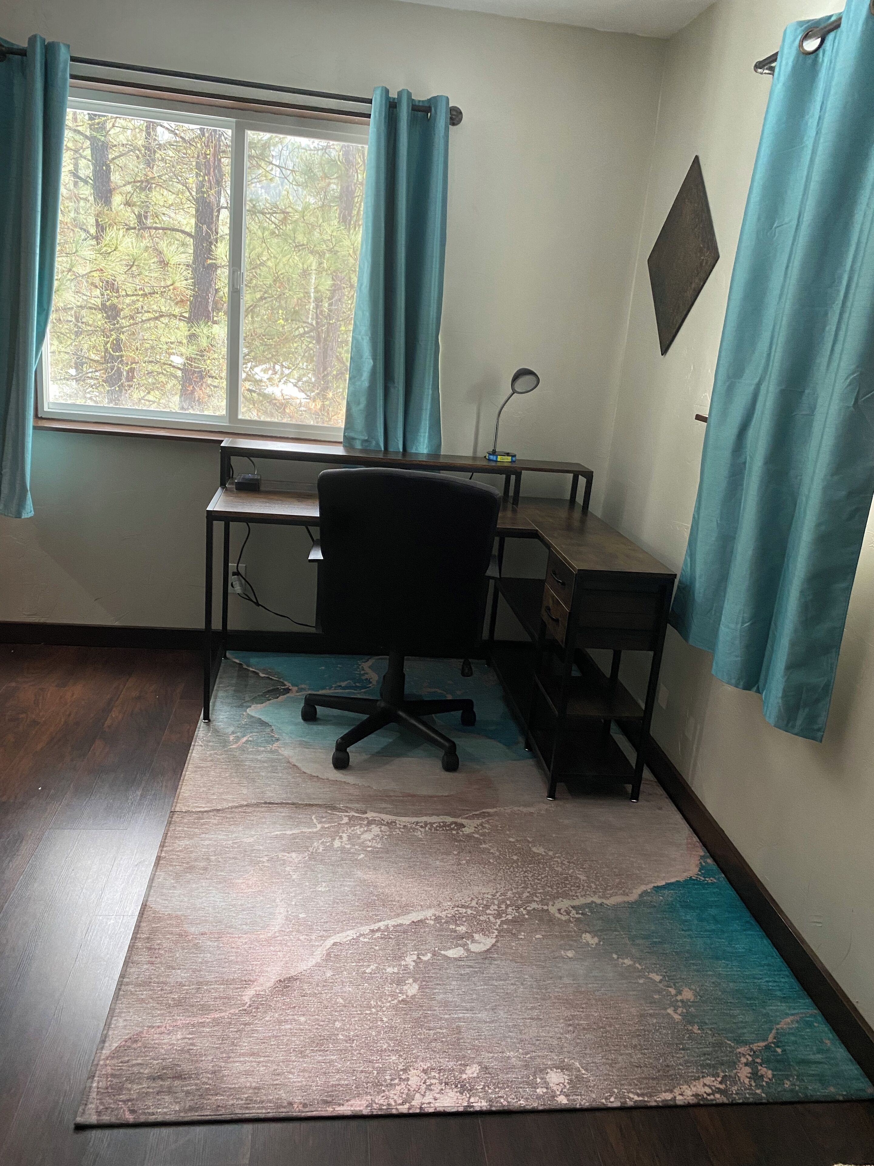 A room with a desk, chair, and a view of trees through a window.