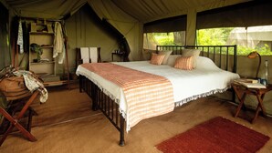A tented accommodation with a large bed, a small table, and a chair. - Esirai Mobile Migration Camp (Serengeti)