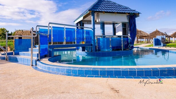 Une piscine avec une terrasse carrelée de bleu, un espace détente couvert et un ciel dégagé.