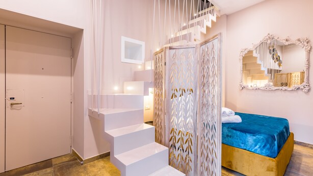 A bedroom with a bed, a white staircase, a wardrobe, and a mirror on the wall. - Golden Terrace at Historical Center (Naples)