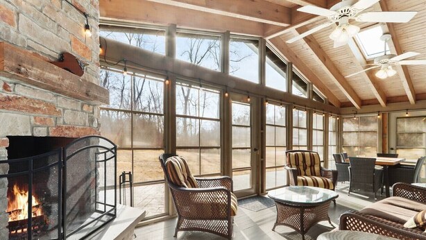 A spacious room with a fireplace, wicker furniture, and large windows offering a view of the outdoors. - Charming Lake Geneva Getaway 4/2 with Hot Tub (Fontana-on-Geneva Lake)