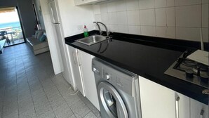 A modern kitchen with white cabinets, a black countertop, and a built-in washing machine. - Keserouane Cozy Apartment With a View (Dbayeh)