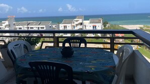 A balcony with a table and chairs, overlooking a coastal view with buildings and the sea. - Keserouane Cozy Apartment With a View (Dbayeh)