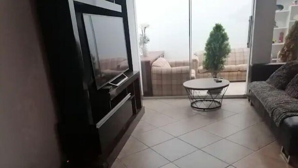 Una sala de estar con televisor, sofá, mesa de centro y vistas a través de un ventanal.