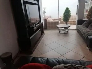 Una sala de estar con televisor, sofá, mesa de centro y vistas a través de un ventanal.