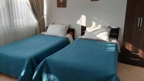 Una habitación con dos camas individuales, un armario de madera y una ventana con cortinas.