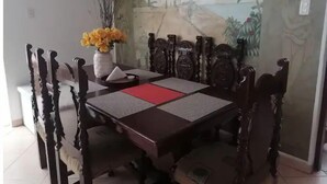 Un comedor con una mesa y sillas de madera oscura, un jarrón con flores amarillas y un mural en la pared.