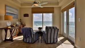 A room with a view of the ocean, a ceiling fan, a table with a lamp, and two striped chairs. - Oceanfront Condo Beautifully Decorated With Beautiful Ocean Views (New Smyrna Beach)