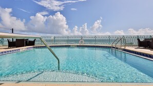 A clear blue pool with a metal railing, lounge chairs, and a view of the sky. - Oceanfront Condo Beautifully Decorated With Beautiful Ocean Views (New Smyrna Beach)