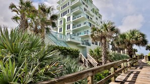A multi-story hotel with balconies, surrounded by palm trees and a wooden boardwalk. - Oceanfront Condo Beautifully Decorated With Beautiful Ocean Views (New Smyrna Beach)