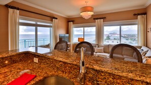 A kitchen with granite countertops, a stainless steel sink, and a view of the sea through large windows. - Oceanfront Condo Beautifully Decorated With Beautiful Ocean Views (New Smyrna Beach)