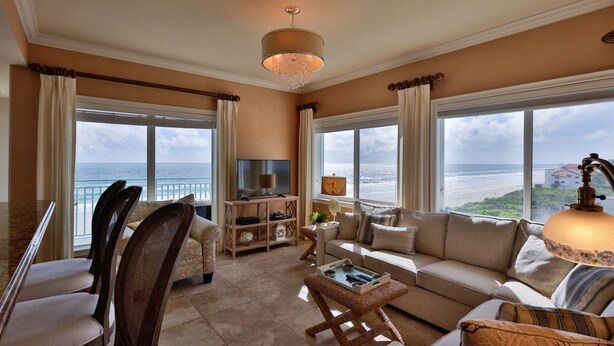 A spacious living room with a large window overlooking the ocean, a television, and a cozy seating area. - Oceanfront Condo Beautifully Decorated With Beautiful Ocean Views (New Smyrna Beach)