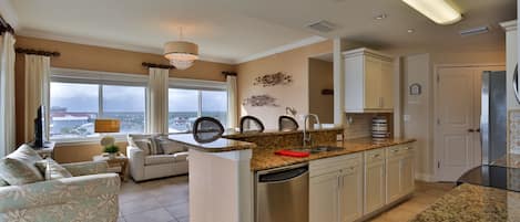 A modern kitchen with a central island, built-in appliances, and a dining area with a sofa and a view of the city.