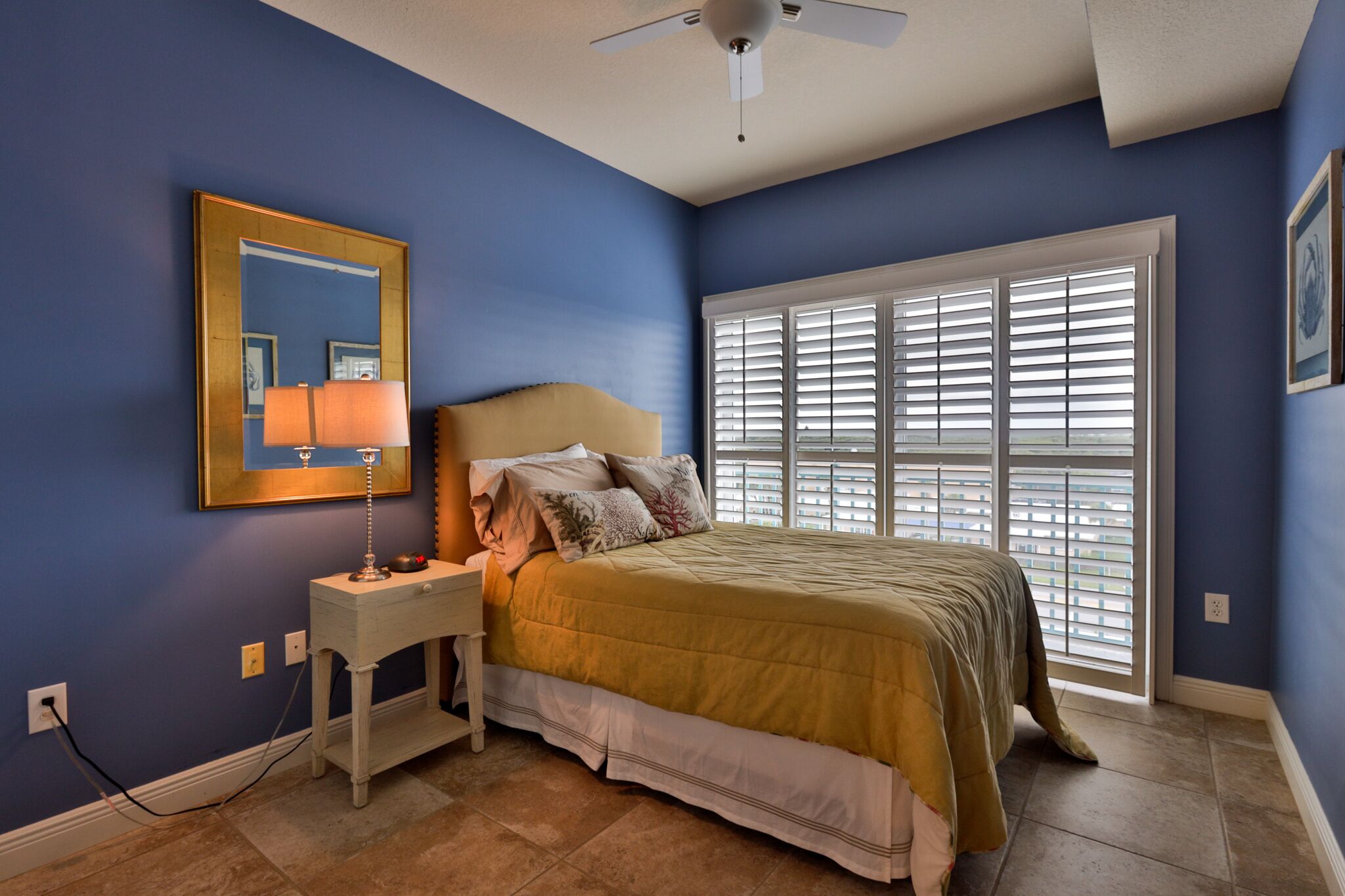 A bedroom with a bed, nightstand, lamp, and a large window with blinds.