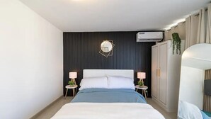 Een moderne slaapkamer met een groot bed, twee nachtkastjes met lampen, een kledingkast en een wandairconditioner.