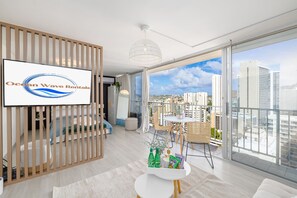 A modern apartment with a large balcony, a TV screen, and a city view. - Stylish, Newly Renovated Condo Near Waikiki Beach (Honolulu)