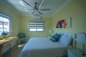 A bedroom with a bed, a desk, a chair, a ceiling fan, and a window with blinds. - Destiny (St. Ann's Bay)