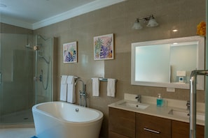 A modern bathroom with a glass-enclosed shower, a freestanding bathtub, a large mirror, and two framed artworks on the wall. - Destiny (St. Ann's Bay)