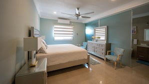 Ein Schlafzimmer mit Bett, Schminktisch, Stuhl, Deckenventilator und Jalousien.