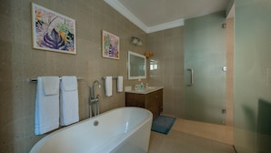 Ein modernes Badezimmer mit freistehender Badewanne, einer Duschkabine aus Glas und zwei gerahmten Kunstwerken an der Wand.