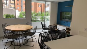 A modern kitchen with a round wooden table, black wireframe chairs, and a large window offering a view of a brick building and greenery. - 3BR magical aparment in the heart of Medellin - Poblado  (Medellín)
