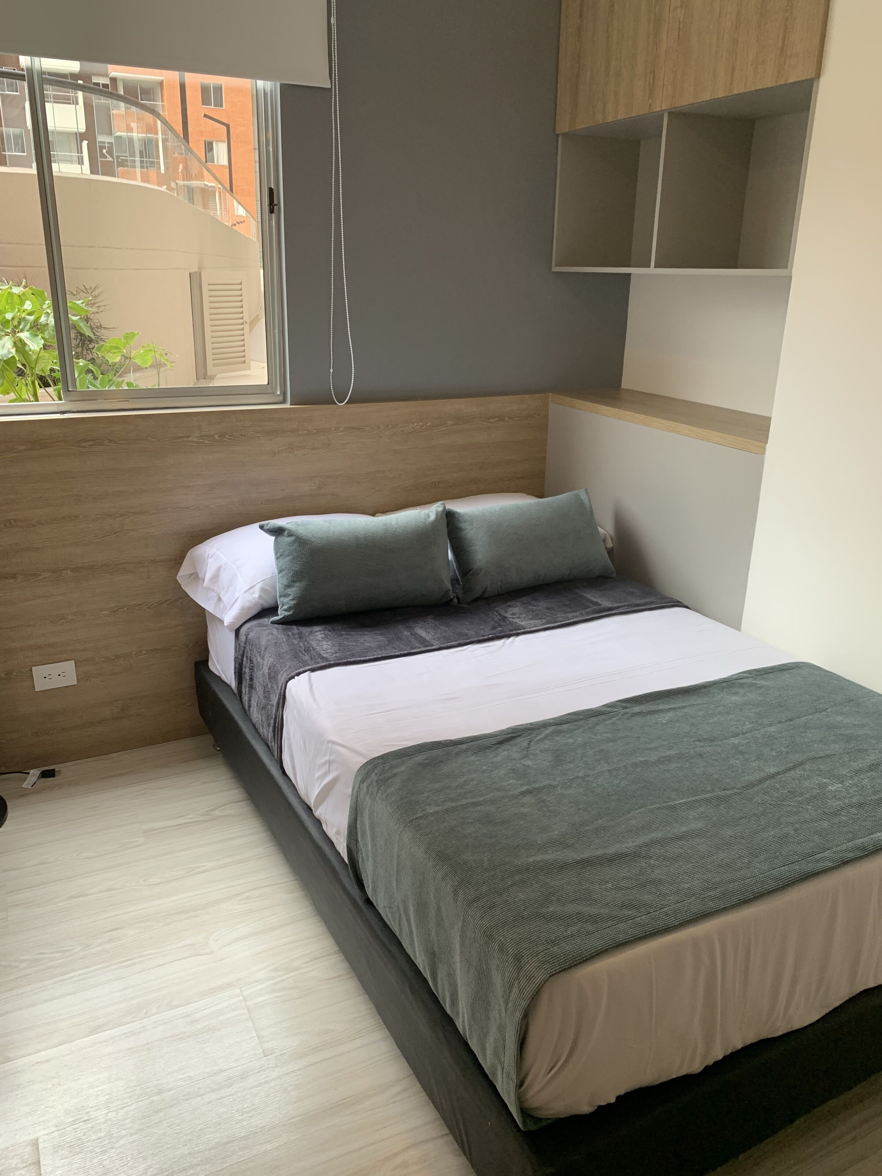 Une chambre à coucher avec un lit, une fenêtre, une tête de lit en bois et une étagère.