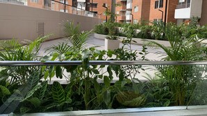 A balcony with lush green plants and a view of a multi-story residential building. - 3BR magical aparment in the heart of Medellin - Poblado  (Medellín)