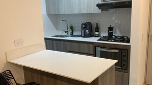 A compact kitchen with a white countertop, a built-in microwave, a gas stove, and a sink. There are two black wicker chairs at the counter. - 3BR magical aparment in the heart of Medellin - Poblado  (Medellín)