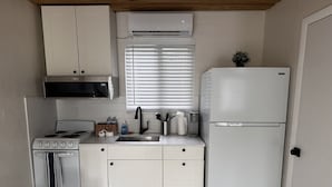 Een kleine keuken met witte kastjes, een kookplaat, een spoelbak en een koelkast.