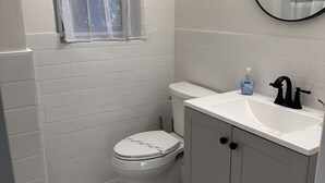 Een badkamer met toilet, wastafel, spiegel en raam met dunne gordijnen.
