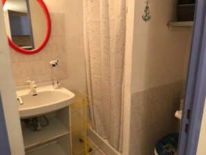 Bathroom features a sink, mirror, shower curtain, and a shelf with storage.