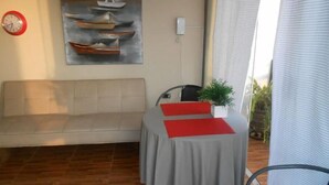 Una habitación con un sofá, una mesa con un cojín rojo, un reloj y un cuadro de barcos en la pared.