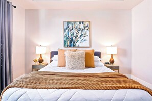 Un lit bien fait, recouvert d’une couverture marron, avec deux lampes de chevet et un tableau accroché au-dessus du lit.
