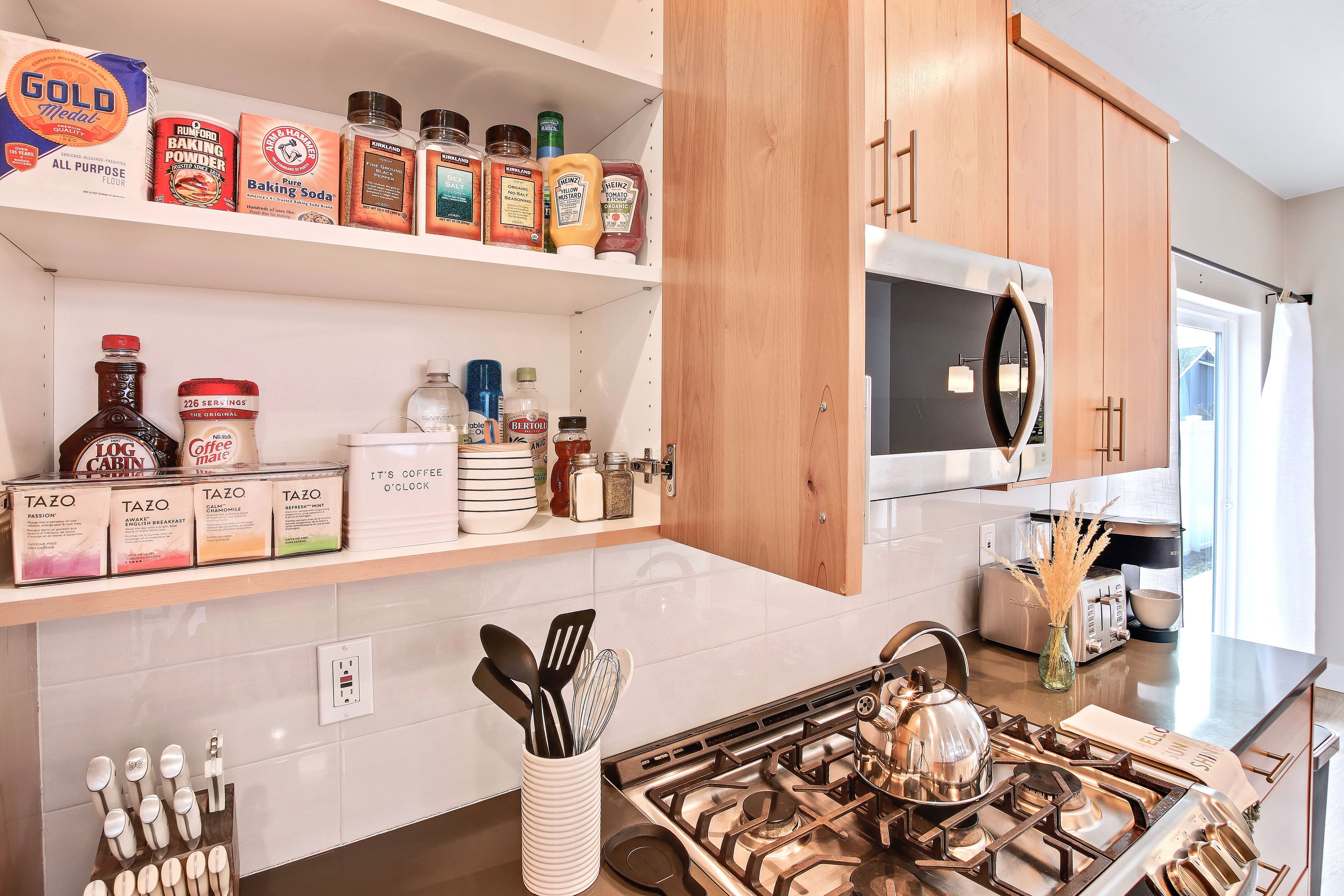 Una cocina con estufa a gas, microondas y varios utensilios de cocina en estantes.